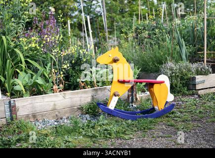 Cheval à bascule en bois dans le jardin. Les enfants vintage jouent à cheval devant des lits de jardin envahis par la végétation. Concept pour l'éducation à la nature, l'école immersive ou l'enfance Banque D'Images