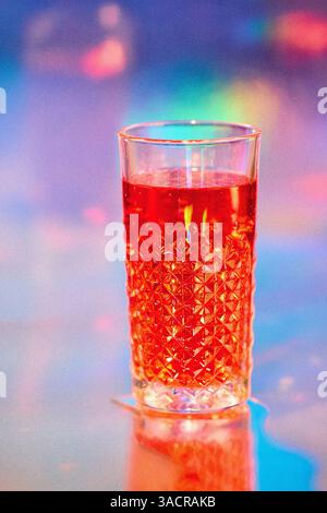 boisson rouge dans un verre à cocktail moderne sur un fond brillant lumineux coloré dans une discothèque ou un bar de plage, grain de film ajouté, mise au point sélective Banque D'Images