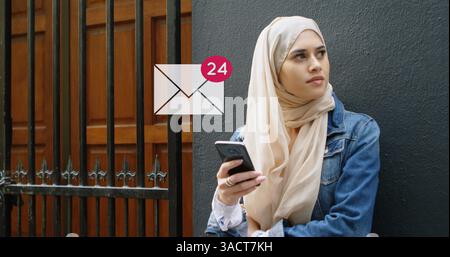 Tenant smartphone, femme en hijab vérifiant les messages à l'extérieur, regardant réfléchi Banque D'Images