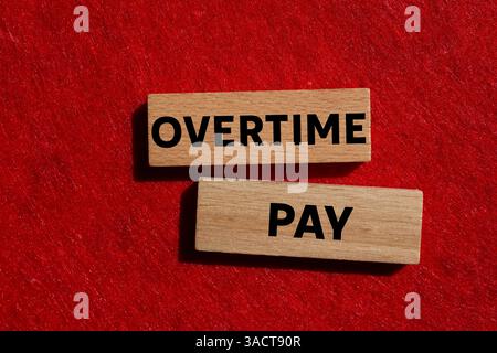 Message de paie d'heures supplémentaires écrit sur des blocs de bois sur fond rouge. Symbole conceptuel de rémunération des heures supplémentaires. Copier l'espace. Banque D'Images