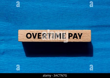 Message de paie d'heures supplémentaires écrit sur bloc de bois sur fond bleu. Symbole conceptuel de rémunération des heures supplémentaires. Copier l'espace. Banque D'Images