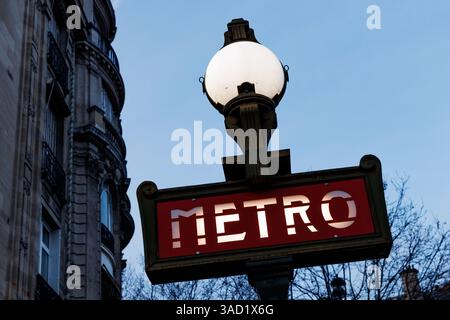 Un panneau rouge et blanc avec le mot Metro écrit dessus. Le panneau est allumé la nuit Banque D'Images