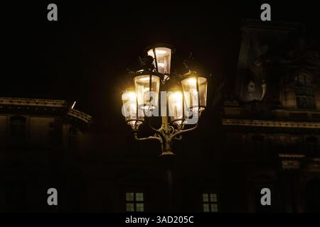 Un lampadaire avec cinq lumières est allumé la nuit. La lumière brille sur un bâtiment Banque D'Images