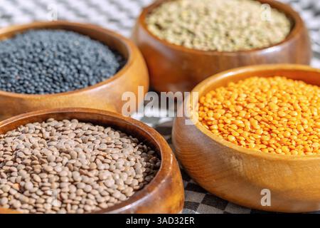 4 types de lentilles dans des bols en bois : lentilles de montagne, lentilles rouges, lentilles béluga, lentilles assiettes Banque D'Images
