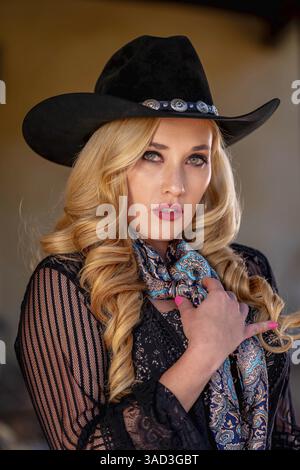 Une belle et confiante femme blonde dans une tenue de cow-boy classique se tient haute, posant avec un pistolet brillant sur sa hanche et un fusil reposant sur son shou Banque D'Images