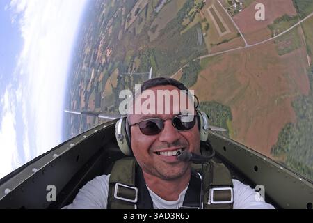 Un pilote de la seconde Guerre mondiale capture un selfie audacieux en plein vol, exécutant des manœuvres aériennes précises dans un avion de chasse classique. Le cockpit vintage et le ciel flou, casquette Banque D'Images