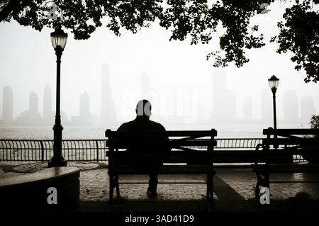 Silhuete d'un homme assis sur un banc avec vue de Manhattan ville en arrière-plan, New York, États-Unis Banque D'Images