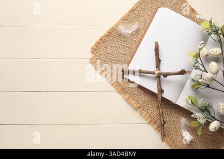 Croix faite de bâtons avec livre blanc et belles fleurs sur fond de bois blanc. Fête de Pâques Banque D'Images