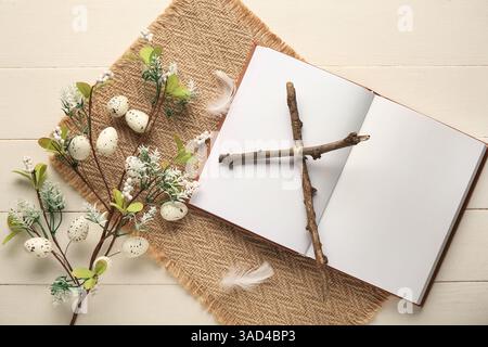 Croix faite de bâtons avec livre blanc et belles fleurs sur fond de bois blanc. Fête de Pâques Banque D'Images