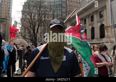 Un manifestant portant une écharpe sur son visage tient un drapeau palestinien lors d'une manifestation pro-palestinienne devant la Bibliothèque publique de New York. Des manifestants pro-palestiniens à Manhattan, New York, ont condamné les Forces de défense israéliennes pour leurs opérations militaires à Gaza. Les manifestants, dont certains sont des étudiants, ont demandé aux universités de rompre leurs relations d'affaires avec l'État d'Israël. Israël a déclaré qu'il allait étendre sa campagne militaire à Gaza et commencer à ajouter de vastes territoires à Gaza aux zones de sécurité d'Israël. Banque D'Images