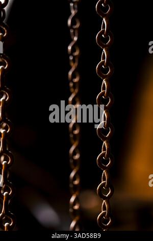 Une étude rapprochée de chaînes métalliques interconnectées suspendues en basse lumière, révélant des bords rouillés et une patine industrielle Banque D'Images