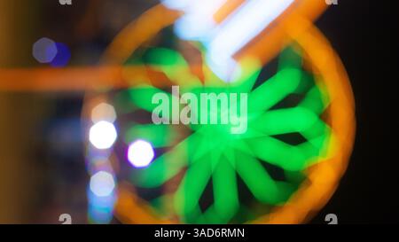 Flou abstrait coloré d'une grande roue la nuit, avec des lumières vertes, orange et blanches brillantes dans un effet bokeh, créant un rêve et artistique Banque D'Images