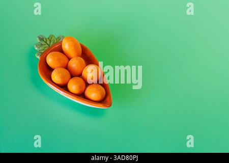Nature morte sur le thème de Pâques avec des œufs orange dans une assiette en forme de carotte sur un fond vert pastel Banque D'Images