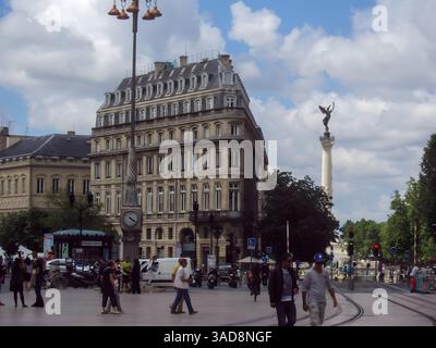 Une scène urbaine animée avec un bâtiment historique à l'architecture ornée, une tour de l'horloge et un grand monument surmonté d'une statue. Le ciel est par Banque D'Images