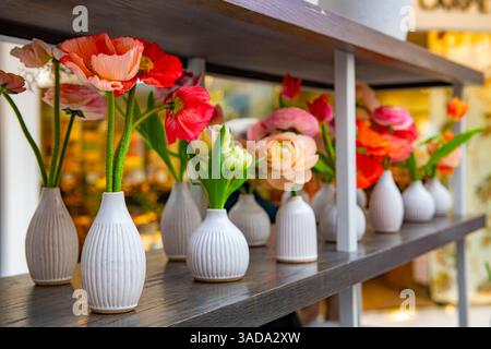 Une belle exposition de coquelicots islandais et de ranoncule dans des vases blancs dans une rangée Banque D'Images