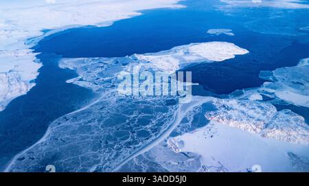 Vue aérienne d'un paysage gelé avec des calottes de glace fissurées et un terrain enneigé. Banque D'Images