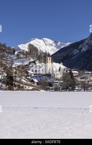 Vue du village de Graun avec église et panorama de montagne en hiver, lac gelé Reschen, Vinschgau, Tyrol du Sud, Italie, Europe Banque D'Images