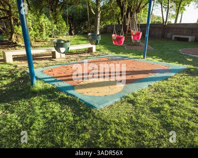 Quatre balançoires pour tout-petits dans un parc calme avec des arbres et la lumière chaude du soleil du soir. Banque D'Images