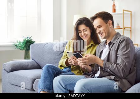 Heureux couple de famille utilisant leurs smartphones pour se montrer quelque chose de drôle sur l'écran. Banque D'Images