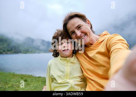 Maman et garçon heureux prenant selfie contre le lac et les montagnes Banque D'Images