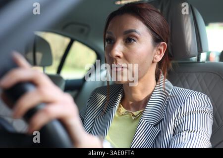 fille en costume d'affaires dans la voiture jurant à un autre conducteur ou piéton, stress, debout dans les embouteillages, trafic congestionné Banque D'Images