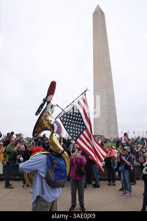 Protestation contre la politique du président américain Donald Trump à Washington, États-Unis - 05 avril 2025. Un homme joue de la musique avec un drapeau américain à l'envers accroché à son instrument alors qu'il prend part à une manifestation Hands Off contre la politique du président américain Donald Trump et de son conseiller, le PDG de Tesla Elon Musk, sur le National Mall à Washington, DC, le 5 avril 2025. Des milliers de personnes sont descendues dans le National Mall de Washington et se sont rassemblées dans d'autres villes à travers les États-Unis et à l'étranger pour s'opposer aux politiques de Trump, dans les plus grandes manifestations depuis son retour à la présidence. WASHINGTON D. Banque D'Images