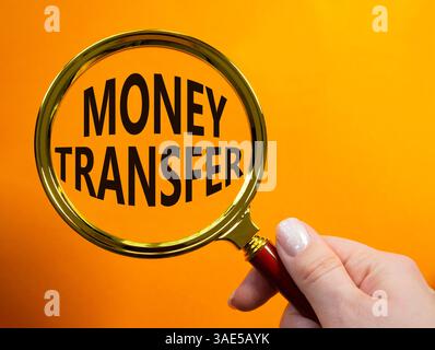 Symbole transfert d'argent. Loupe avec mot concept transfert d'argent. Main d'homme d'affaires. Beau fond orange. Entreprise et transfert d'argent c Banque D'Images