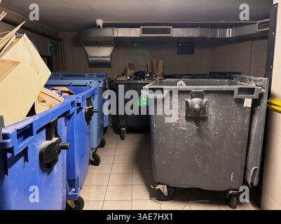 Station intérieure de tri des déchets avec de grands bacs. Une salle de collecte des déchets intérieure faiblement éclairée, dotée de plusieurs grands conteneurs pour la séparation des déchets. Banque D'Images