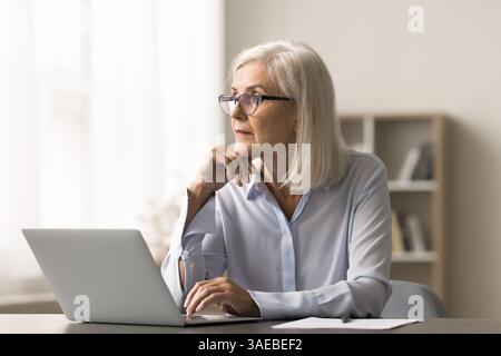 Pensive femme d'affaires d'âge moyen créer des plans distrait de l'écran de carnet Banque D'Images