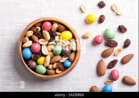 Rainbow trail mix dans un bol en bois sur tissu de lin. Un mélange de collation de cacahuètes au chocolat au lait enrobées de bonbons, de cacahuètes grillées, de raisins secs et d'amandes grillées. Banque D'Images
