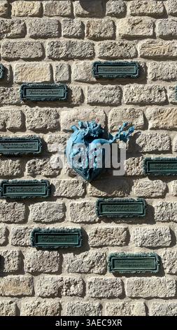 Un cœur sculpté avec des détails floraux est monté sur un mur de pierre texturé, entouré de plaques encadrées avec des inscriptions multilingues. L'art urbain rencontre Banque D'Images