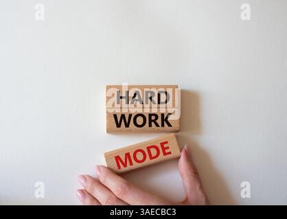 Symbole du mode de travail acharné. Mot concept mode de travail dur sur des blocs de bois. Main d'homme d'affaires. Beau fond blanc. Concept de mode de travail professionnel et dur Banque D'Images