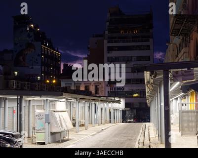 Athènes, Grèce - 5 avril 2025 : illuminé les stands vides du marché municipal central Varvakios et les bâtiments de la ville contre un ciel sombre Banque D'Images