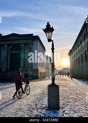 Coucher de soleil à Copenhague près du Palais Christianborg. Une personne marchant un vélo et un lampadaire antique. Un jour d'hiver, enneigé avec un ciel bleu clair. Banque D'Images