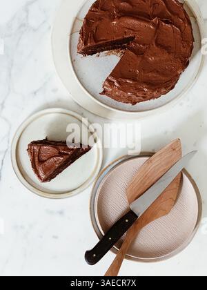 vue de dessus d'un gâteau au chocolat riche avec glaçage crémeux, une tranche coupée sur le côté et des ustensiles de service Banque D'Images