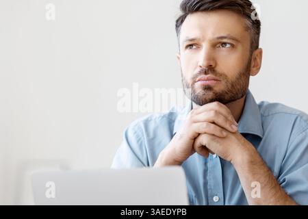 Portrait d'un homme d'affaires pensif assis sur un lieu de travail avec un ordinateur portable et Vue sur l'extérieur Banque D'Images