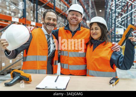 Les ouvriers des entrepôts et leur gestionnaire se sourient et se serrent dans les bras, célébrant une collaboration réussie dans leur centre logistique Banque D'Images