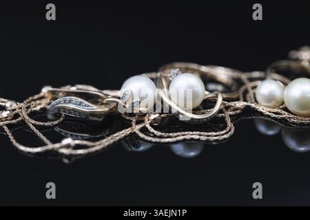 Les boucles d'oreilles et les bagues dorées ornées de perles blanches se trouvent sur une surface noire du miroir Banque D'Images