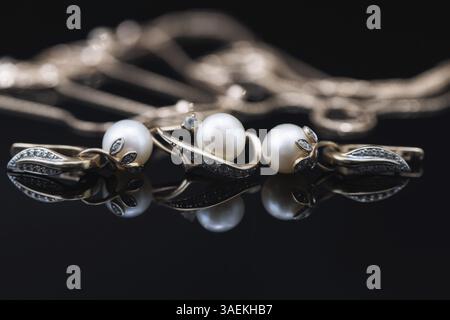 Les boucles d'oreilles et les bagues dorées ornées de perles blanches se trouvent sur une surface noire du miroir Banque D'Images