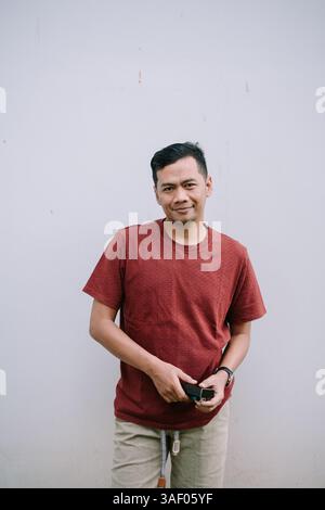 Homme asiatique souriant dans la chemise couleur brique posant devant le mur Uni. Portrait confiant et décontracté. Banque D'Images