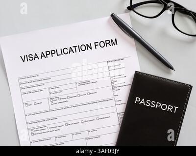 Formulaire de demande de visa avec passeport, stylo et lunettes posées sur la table grise, se préparant au remplissage Banque D'Images