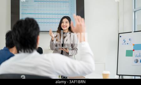 Femme d'affaires ou employée de bureau féminine regarde un collègue masculin qui a levé la main pour poser une question. Homme d'affaires et femme a une réunion à offi Banque D'Images