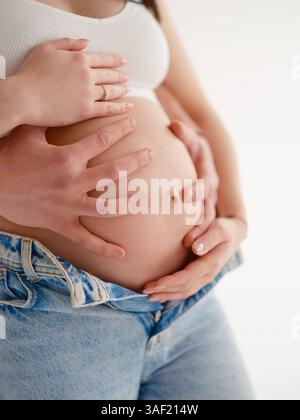 Gros plan d'une femme enceinte et de son homme tenant doucement son ventre. Tendre moment d'amour, de soins et d'anticipation de la parentalité. Maternité, paternité Banque D'Images