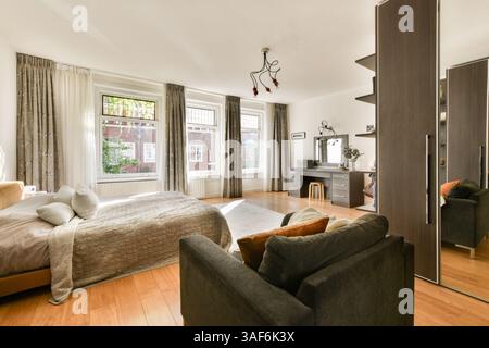 Une chambre bien conçue avec un lit confortable, un mobilier élégant et une lumière naturelle abondante créant une atmosphère chaleureuse et accueillante. Banque D'Images