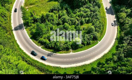 Vue aérienne de la route sinueuse à travers la forêt verdoyante. Une vue aérienne d'une route courbe serpentant à travers une forêt dense et verdoyante, avec plusieurs voitures Banque D'Images