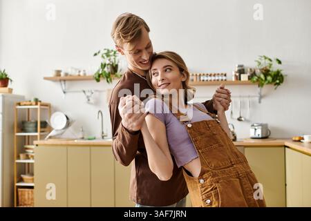 Un jeune couple danse joyeusement ensemble dans leur cuisine confortable. Banque D'Images