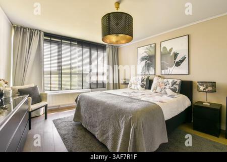 Une chambre moderne magnifiquement conçue avec un lit confortable, un décor élégant et une lumière naturelle abondante diffusant à travers de grandes fenêtres. Banque D'Images