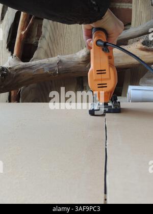 à l'aide d'une scie sauteuse pour couper des feuilles minces de contreplaqué ou de bois ou des feuilles épaisses de carton le long d'une ligne, atelier de menuiserie avec des matériaux artisanaux et des outils à main Banque D'Images