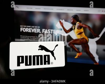 Stuttgart, Allemagne - 11-20-2024 : personne tenant un smartphone avec le logo de la société allemande de chaussures et de vêtements Puma se sur l'écran devant le site Web. Banque D'Images