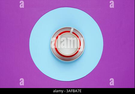 Tasse en céramique rétro sur un fond violet avec un cercle bleu au milieu. Natures mortes de mode à plat. Vue de dessus Banque D'Images